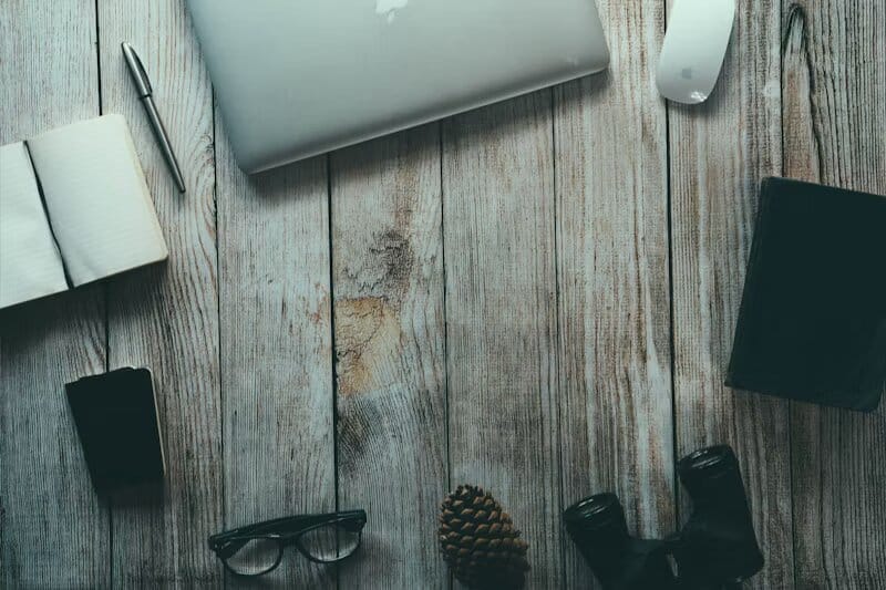 Scrivania in legno con laptop, libro, telefono e penna appoggiati sopra.